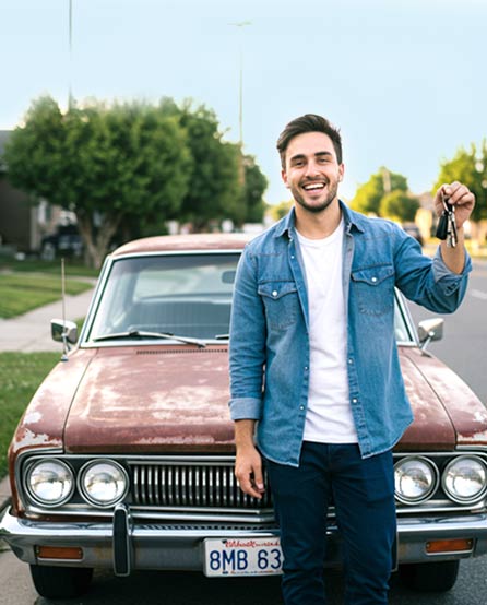 Man holding keys in front of a junk car