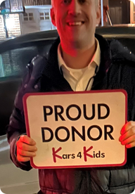 A person holding a sign that says Proud Donor Kars4Kids