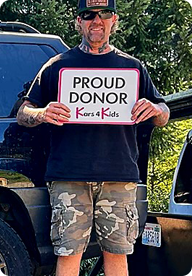 A person holding a sign that says Proud Donor Kars4Kids
